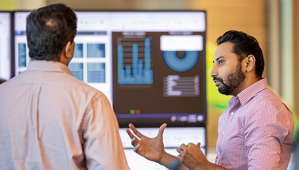 Two men speaking in front of a graph display