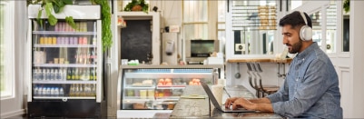 A person in headphones works on a laptop at a café.