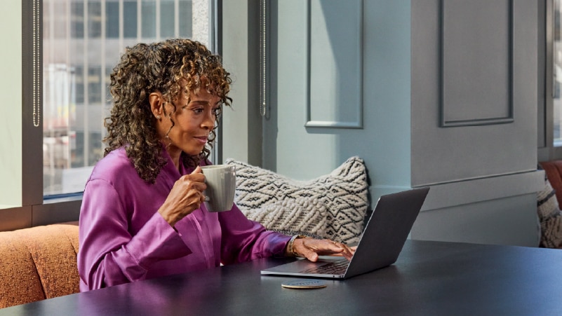 A person holding a coffee mug types on a laptop.