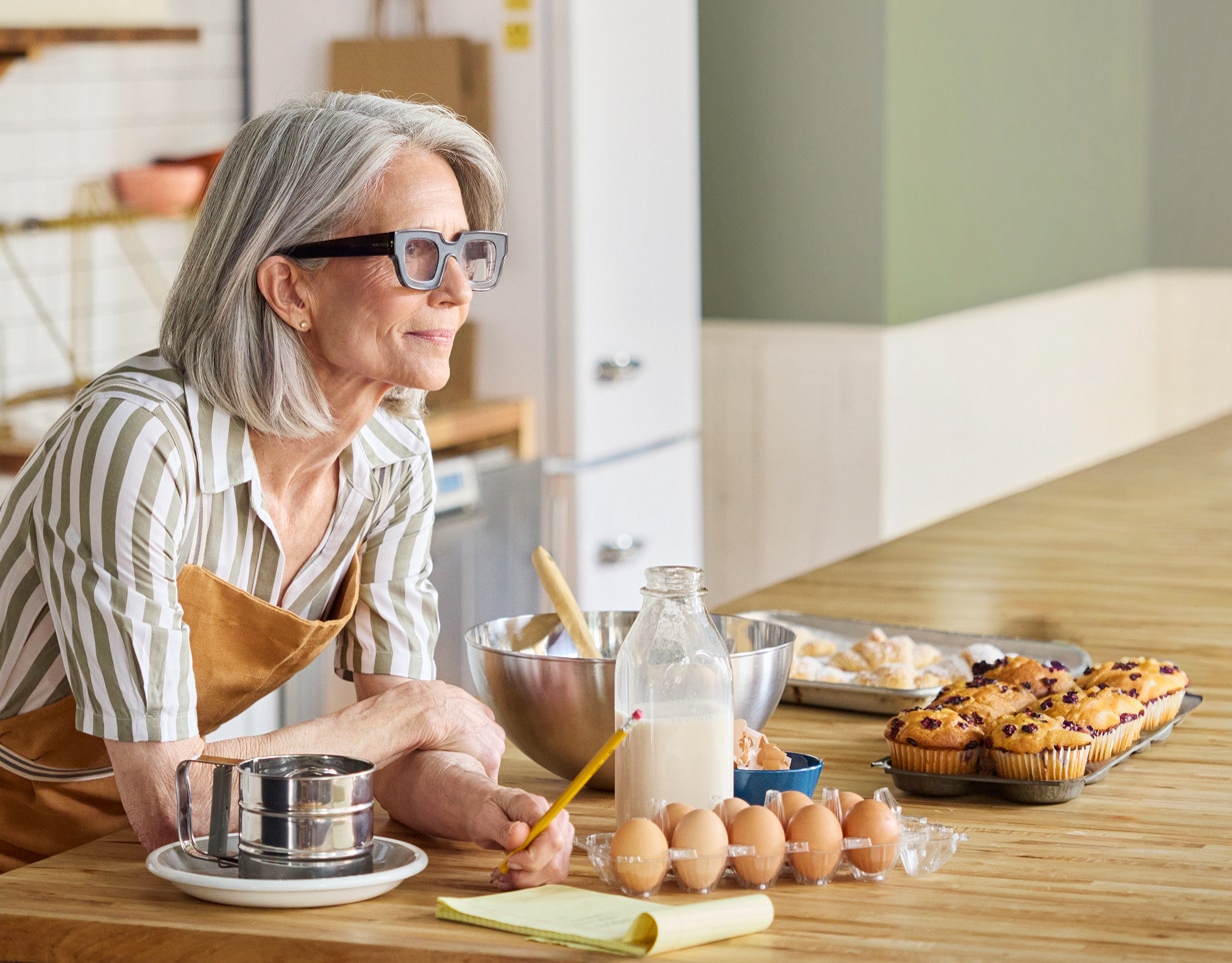 A Schwab participant baking in their kitchen with eggs, milk, mixing bowls, and muffins on the counter.