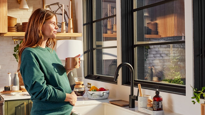 A pregnant woman enjoying a cup of coffee in her kitchen, looking out the window.