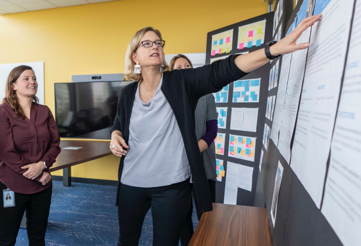 A person gestures toward a poster board while two other people look on.