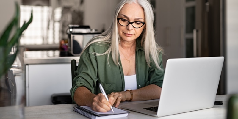 A person sits in front of a computer writing in a notebook.