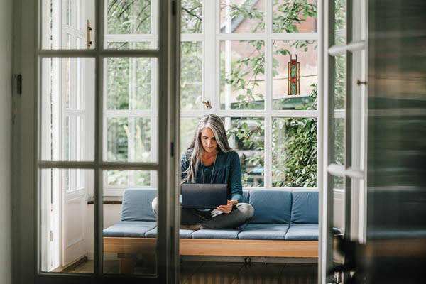  Lady with long gray hair sitting on a blue couch looking at a lap top screen