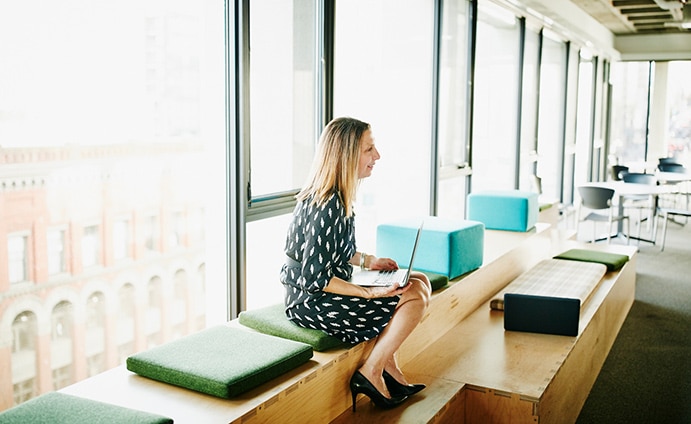 Woman sitting on bench inside with a laptop