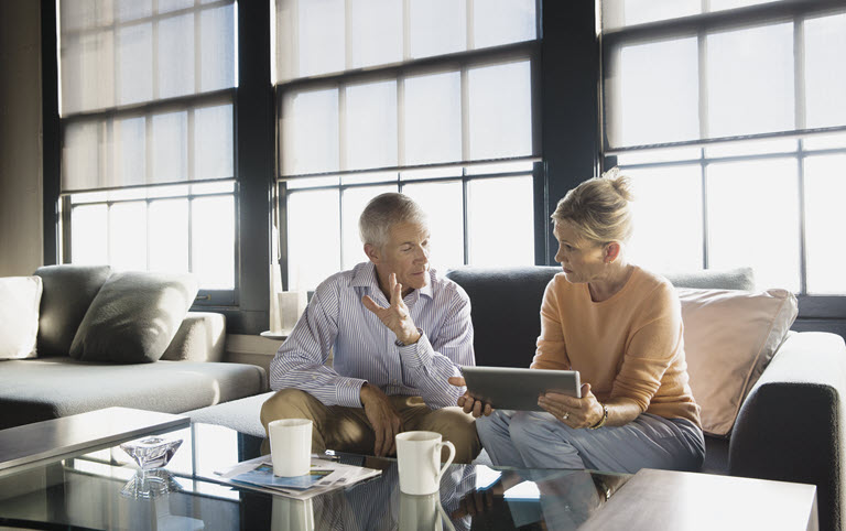 Man and woman sitting on a couch looking at a tablet screen while talking