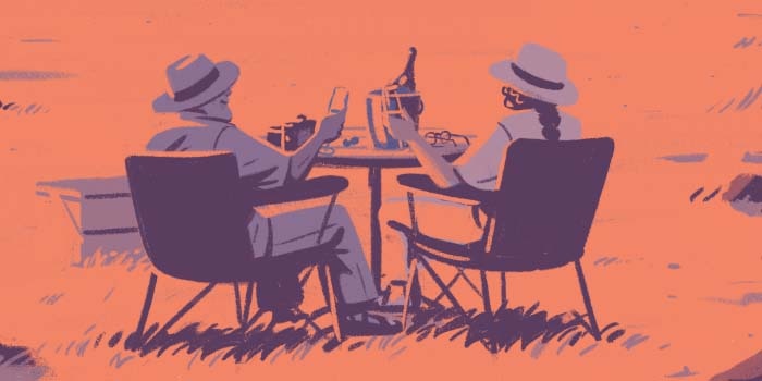 An older couple sharing a bottle of wine outdoors while camping.