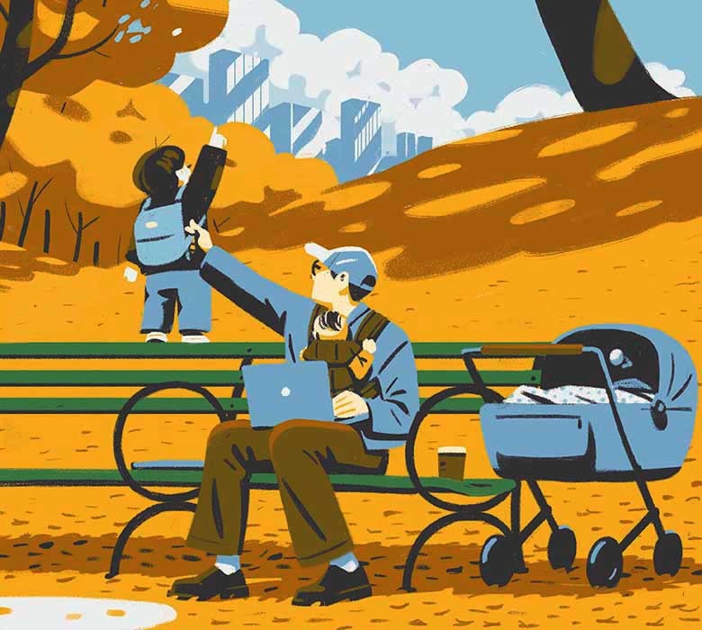 A young father sits on a park bench with an infant strapped to his chest and laptop on his lap while steadying his toddler who is standing on the back of the bench.