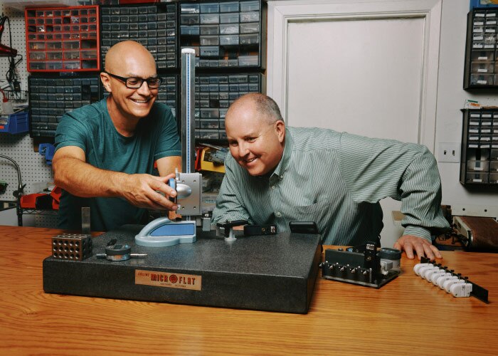Two men working together at a table with technical equipment, calibrating sensors on an AI-powered tree-monitoring device.