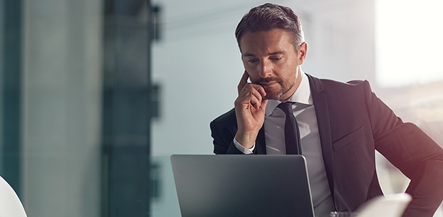 Business person looking at a laptop with a pensive expression.