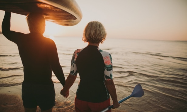Two kayakers hold hands while walking into the water at sunset.